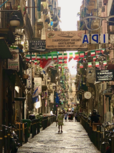 A narrow street in Naples lined with colorful buildings and vibrant signs capturing the city's lively atmosphere.